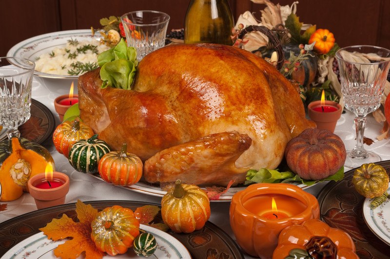 This photo shows a table set for Thanksgiving dinner, including a large cooked dinner, a bowl of mashed potatoes, elegant dinnerware, and lighted candles in orange containers, representing the best Thanksgiving affiliate programs.