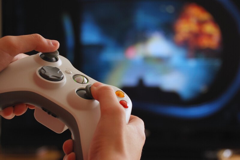 An image of two hands and a game controller, with an out-of-focus screen in the background