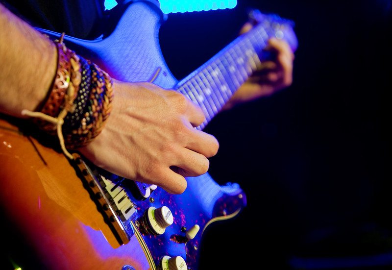 Close up image of a man playing guitar with bracelets on his wrist