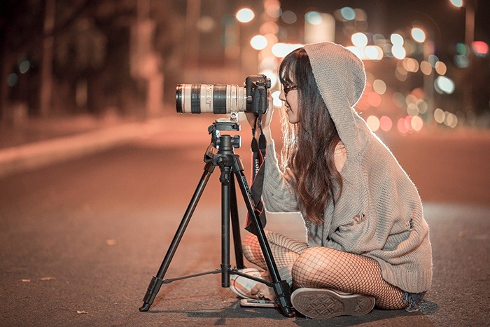 A young woman sitting on the road at night with a camera on a tripod