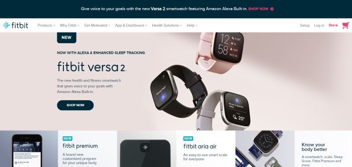 This screenshot of the home page for Fitbit shows three Fitbit Versa 2 smartwatches in pink, black, and gray over a beige background, near a section of black text describing the device, along with a black "shop now" call-to-action button.