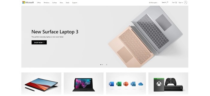 This screenshot of the home page for Microsoft has a gray background with an overhead photo of a pink laptop and keyboard and a gray laptop and black text announcing the new Surface Laptop 3.