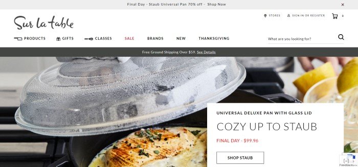 This screenshot of the homepage for Sur La Table has a white navigation bar with black text above a photo of a deluxe pan with cooked chicken inside it, next to a white and black advertisement for the pan.