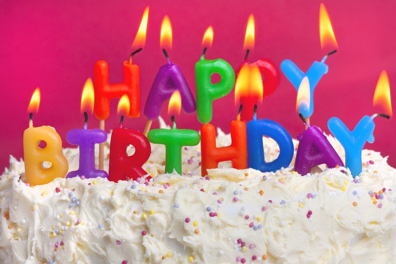 This photo shows a white cake with sprinkles and lit candles in various colors that spell out Happy Birthday in front of a magenta background, representing the best birthday affiliate programs.