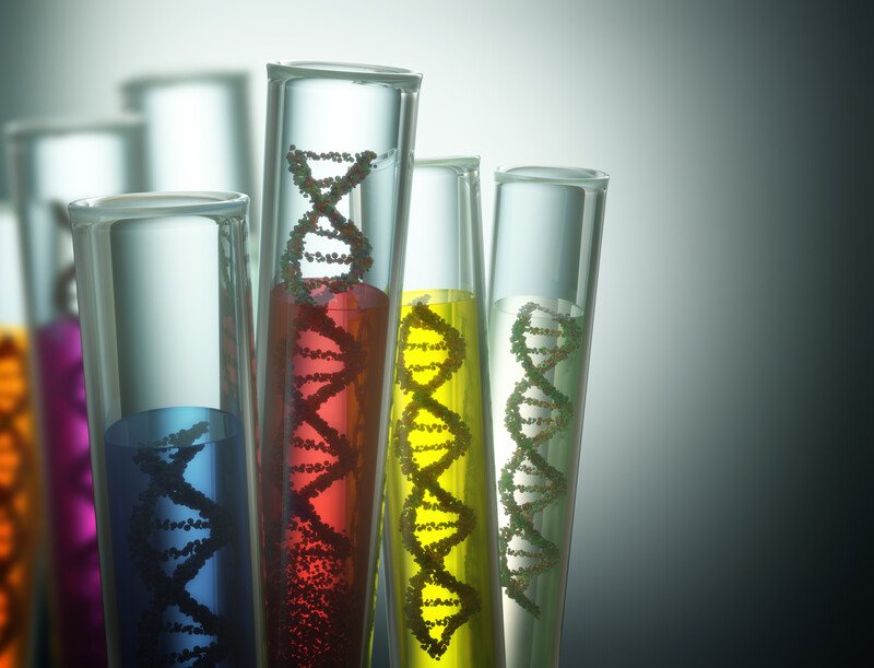 This photo shows a set of five test tubes against a white light and dark background, with each test tube containing strands of DNA in liquid colored maroon, blue, and yellow, representing the best genetic testing affiliate programs.