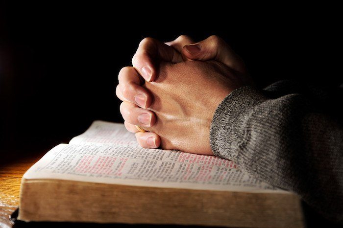 Hands folded in prayer over a bible