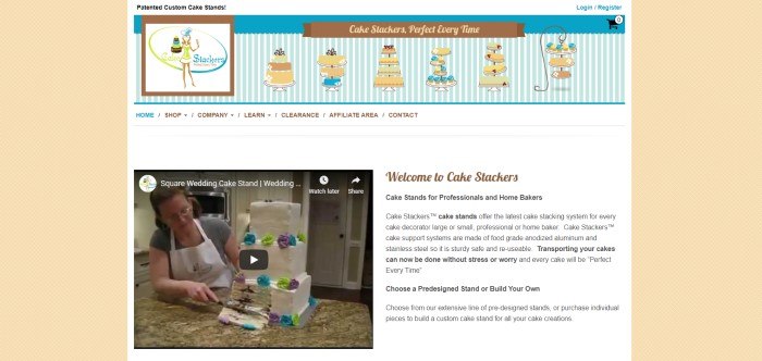 This screenshot of the home page for Cake Stackers has a pale yellow background with tiny white latticework and a main section with a white background, a blue and white striped banner that includes graphics of cakes in brown, blue, and green, a white navigation bar, a video image of a woman cutting a square tiered cake, and text in black and brown that describes what Cake Stackers is all about.