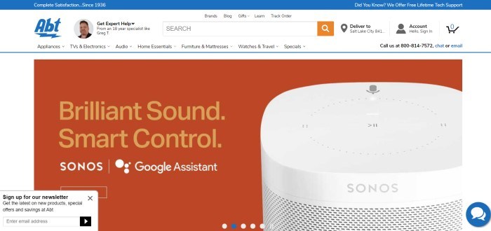 This screenshot of the home page for Abt Electronics has a white background and navigation bar, a blue header, and a large orange area with a photo of a Google assistant named Sonos, along with an advertisement for the Sonos.