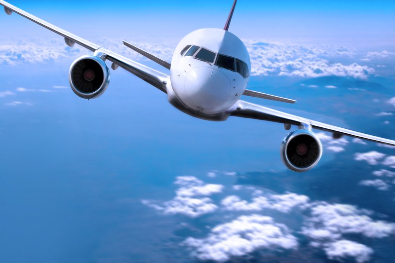 This image shows an oncoming white twin-engine aircraft in a blue sky above white clouds and water, representing the best airline affiliate programs.