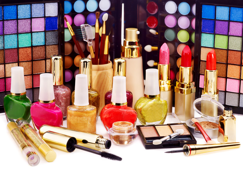 This photo shows a large selection of makeup, including two enormous eyeshadow palettes standing on end, several open lipsticks in shades of red and pink, and a row of nail polish in colors ranging from yellow and green to bright red, representing the best cruelty-free makeup affiliate programs.