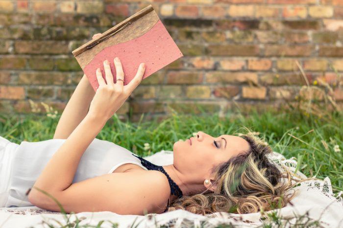 A young woman lying on her back outside reading a book