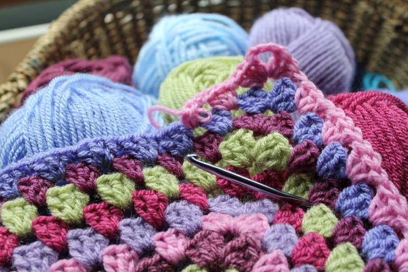 A crocheted blanket with various balls of wool and a crochet hook