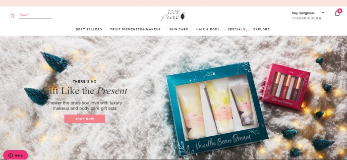 This screenshot of the home page for 100% Pure has a white navigation bar above an overhead photo of 100% pure gift sets lying on what appears to be snow and a pink call-to-action button.