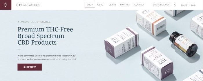 This screenshot of the home page for Joy Organics has a white navigation bar above a light gray section showing small boxes containing Joy Organics products, along with text in black and gray announcing premium THC-free CBD products and a burgundy call-to-action button.