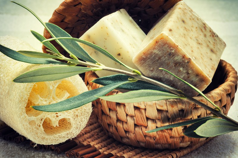 This photo shows two bars of natural home-crafted soaps in a brown basket next to a pale loofah sponge and a sprig of herbs, representing the best natural beauty product affiliate programs.