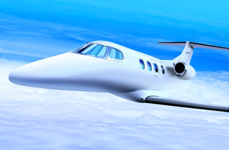 This image shows a white jet flying in a blue sky above the clouds, representing the best private jet charter affiliate programs.