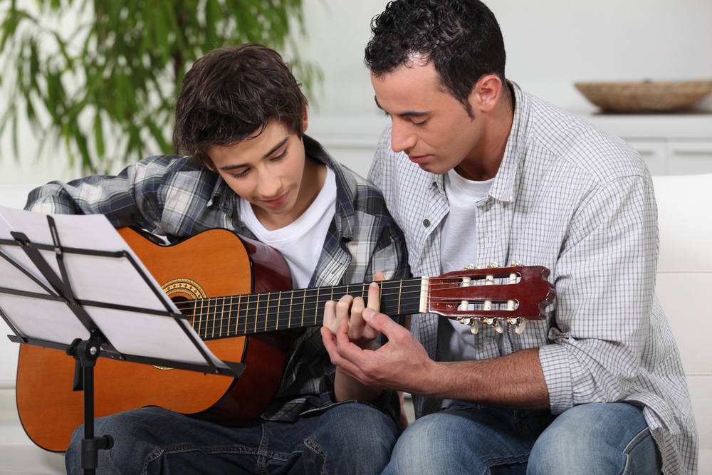 A man teaching a boy how to play guitar