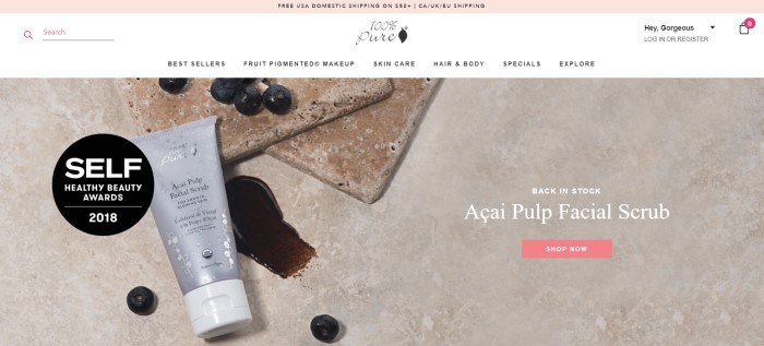 This screenshot of the home page of 100% Pure has a pink header and white navigation bar above a photo of some scattered acai berries and a gray bottle of acai pulp facial scrub on a tan-colored tile background.