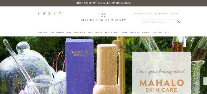 This screenshot of the home page for Living Earth Beauty has a dark header and a white navigation bar above an image of a periwinkle box with gold lettering reading 'Mamalo Skin Care,' as well as a gold-colored bottle, a clear glass, and what appears to be water flowing from a gold-colored pipe outdoors.