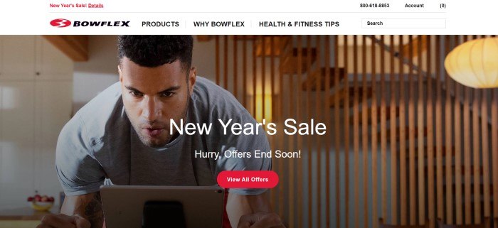 This screenshot of the home page for Bowflex has a white navigation bar with black and red text above a photo of a dark-haired, intensely focused man in gray clothing using an exercise machine in his home, with a wooden divider and stairs in the background, along with white text announcing a New Year's sale and a red call-to-action button.