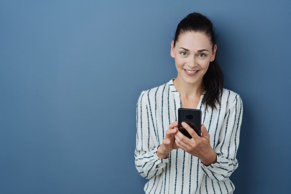 A woman using her phone against a blue background