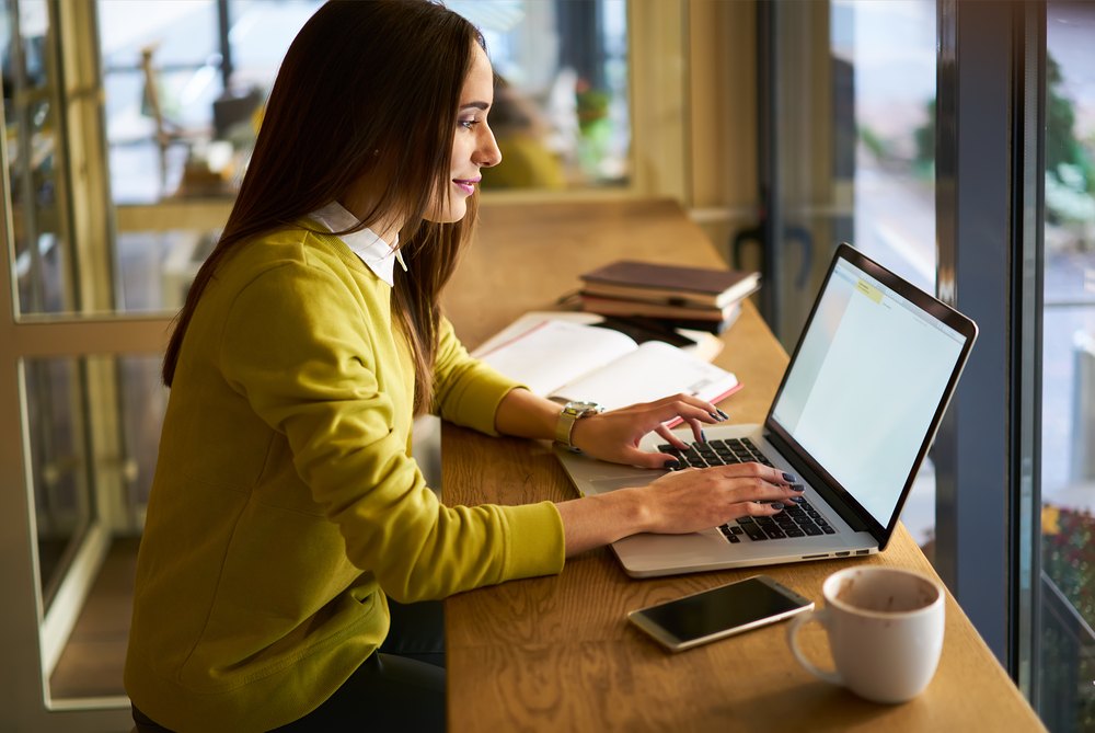 A young woman in a yellow shirt working on her laptop