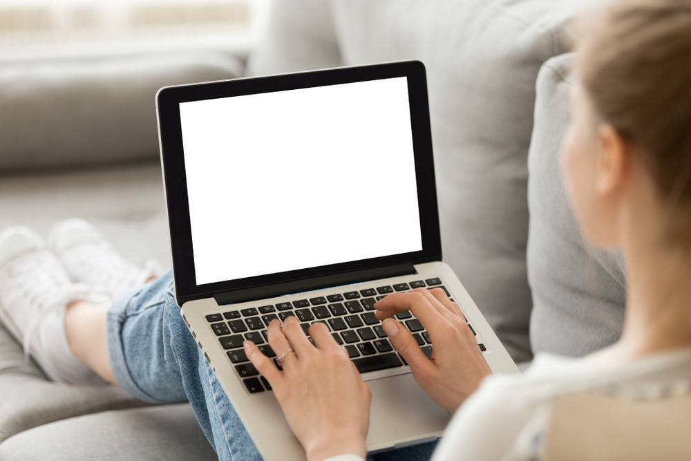 A young woman sitting on the couch typing on her laptop