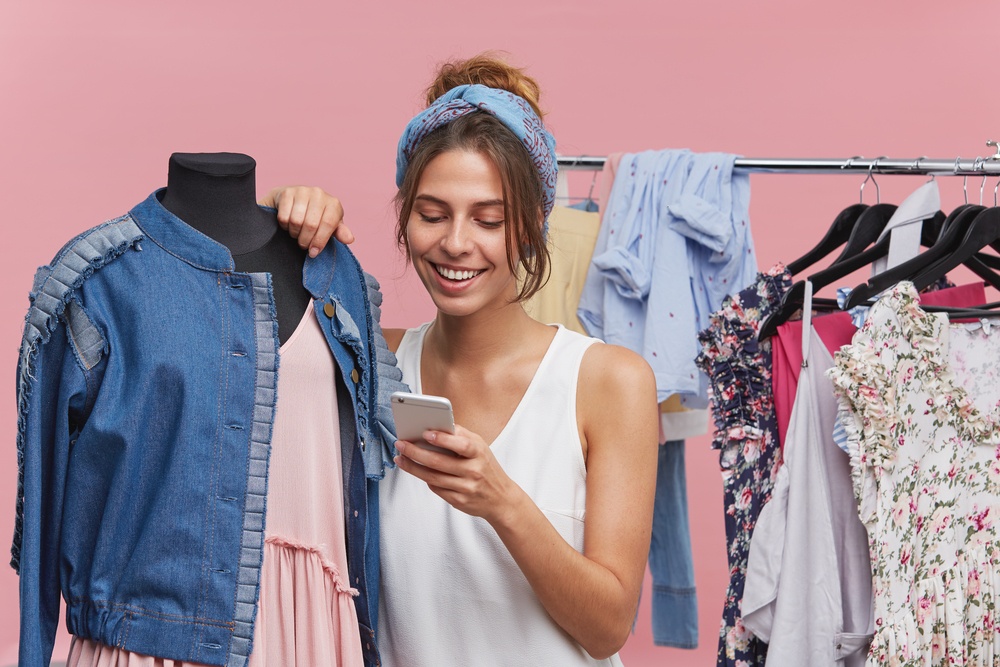 A young woman standing next to clothes racks with her phone in her hand