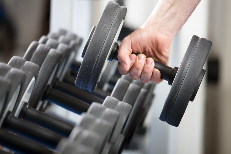 This photo shows a hand pulling a dark gray weight off a rack of hand weights, representing the best workout affiliate programs.