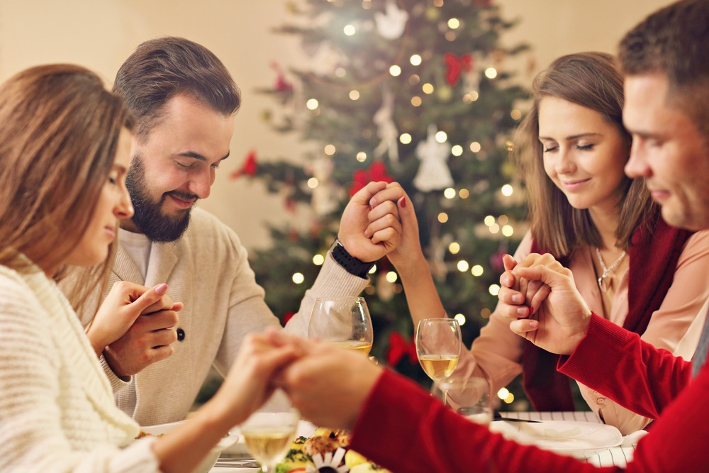 christian friends saying a prayer during the holidays with Christmas tree and decorations