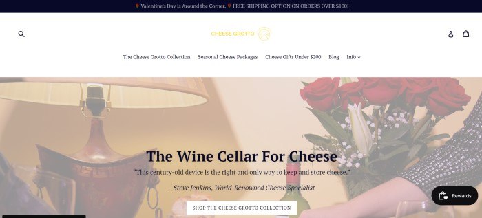 This screenshot of the home page for Cheese Grotto has a black header, a white navigation bar, and a photo showing a lit lamp, red roses, and a serving tray of wine and cheese, along with black text describing cheese grottos as wine cellars for cheeses.