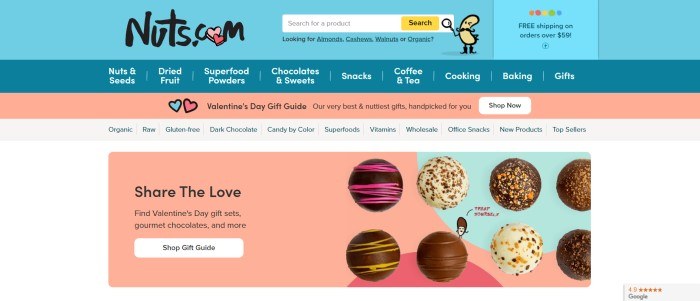 This screenshot of the home page of Nuts.com has a light blue header, a darker blue navigation bar, and coral and aqua elements throughout the page, including a secondary navigation bar and a photo section showing several types of chocolates with black text inviting shoppers to share the love and buy a gift for Valentine's Day.