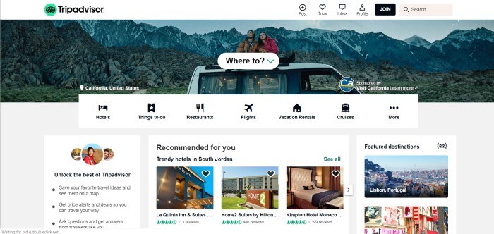 This screenshot of the home page for Trip Advisor has a white header, a banner with a photo of a man in a brown coat and a woman in a red coat sitting on top of a white truck near some jagged mountains, above a white navigation bar and information boxes with black text and pictures inviting visitors to unlock the best of TripAdvisor, find trendy hotels, and visit featured destinations.