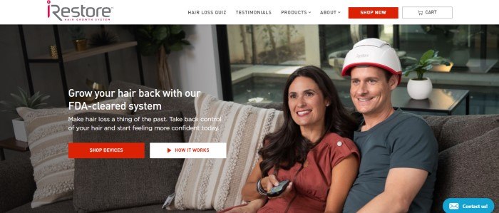 This screenshot of the home page for iRestore Laser shows a smiling woman with brown hair and a russet shirt holding a television remote control in her hand, while she snuggles next to a smiling man in a charcoal-colored tee shirt and an iRestore helmet on a brown and white couch. 