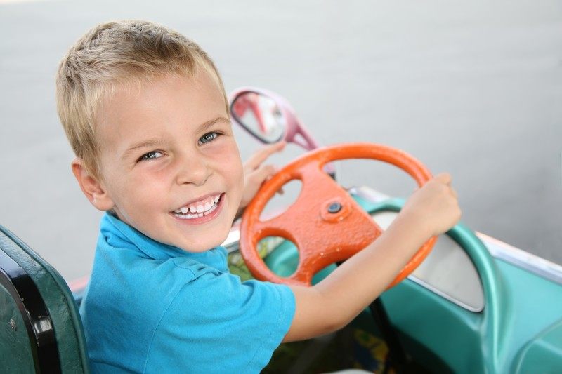 This photo shows a smiling blonde boy in a blue shirt sitting inside a theme park bumper car with an orange steering wheel, representing the best Disney affiliate programs.