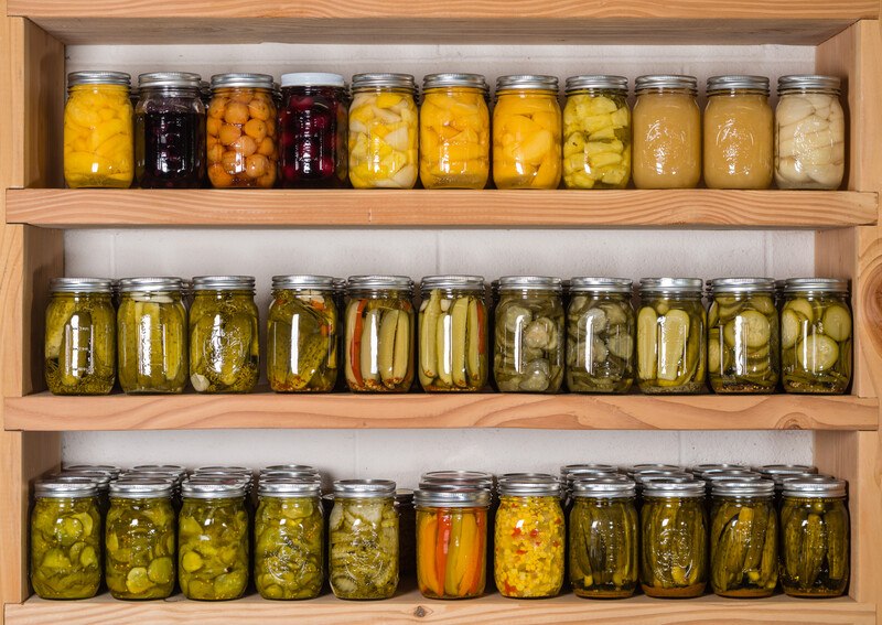 this photo shows three shelves of bottled foods, including pickles and fruits, representing the best food storage affiliate programs.