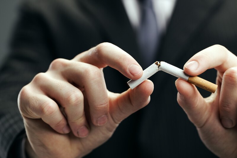 This photo shows the hands of a man in a dark business suit as he breaks a cigarette in half, representing the best quit smoking affiliate programs.