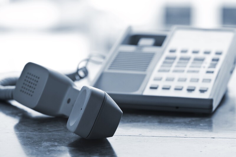 This photo shows a gray telephone handset lying on a table next to the base, representing the best telecom affiliate programs.