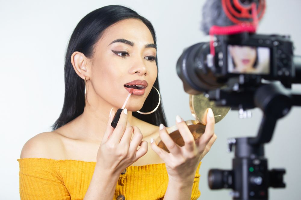 asian beauty guru putting on lipstick in front of the camera recording a video tutorial