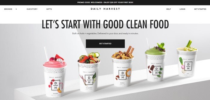 This screenshot of the home page of Daily Harvest has a black header with a promo code, a white navigation bar, and a photo of several cups of Daily Harvest products in a row with a gray background, along with black text announcing clean eating and a black call to action button.