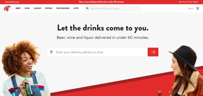 This screenshot of the home page of Drizly has a red header, a white navigation bar, and a photo of two smiling women with drinks in their hands, chatting in front of a red and white background, along with a search bar and black text reading 'Let the drinks come to you.'