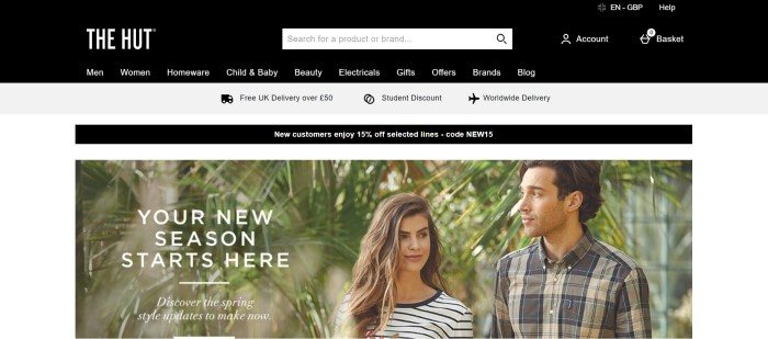 This screenshot of the home page for The Hut has a black search bar and navigation bar, a gray announcement bar for free delivery and student discounts, and a photo of a smiling man and woman in striped and plaid shirts standing in front of tropical plants, along with white text announcing new spring style updates.