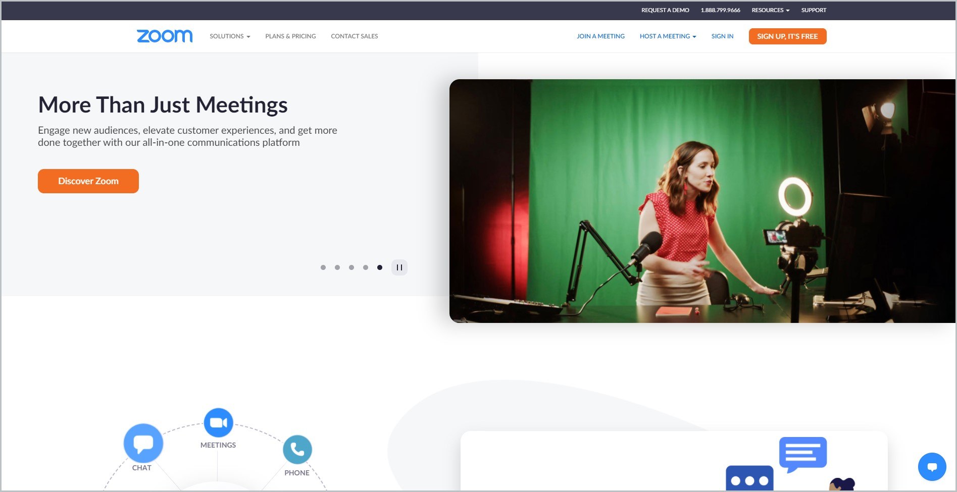 screenshot of Zoom homepage with black announcement bar, with white header bearing the website's name and main navigation menu, it features an image of a woman in red sleeveless top and khaki skirt with microphone and ring light in a video conference