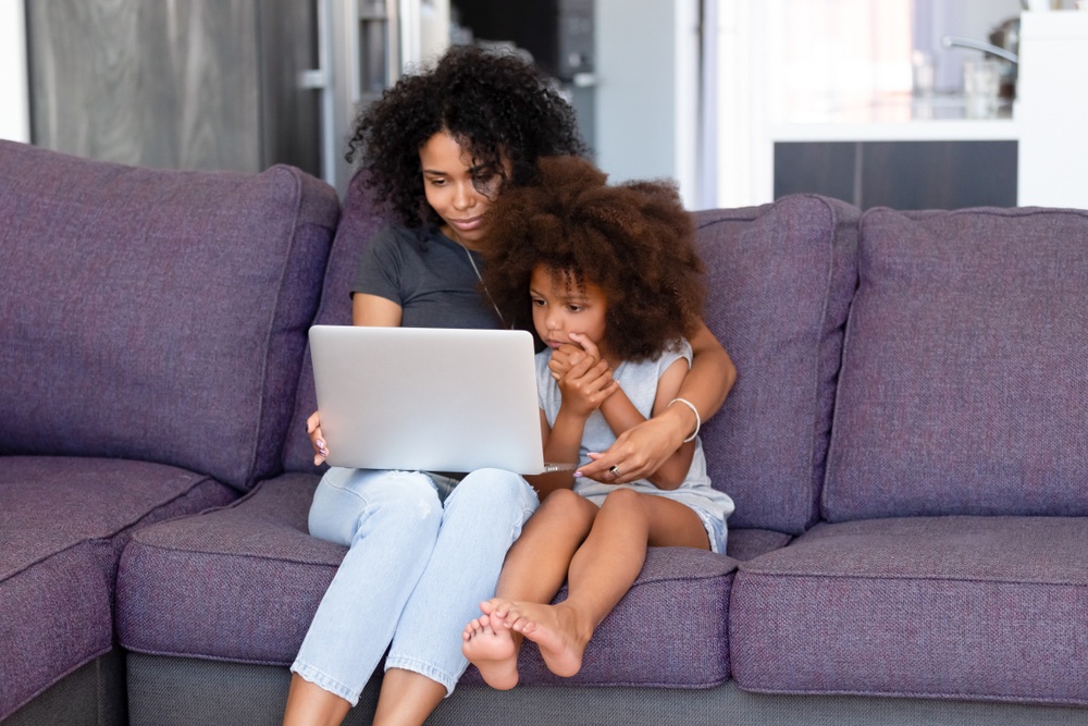 african american mom with young child blogging with laptop on couch