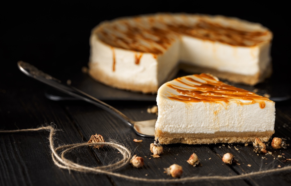 dense cheesecake slice on serving spoon with caramel drizzle and seasalt sprinklers