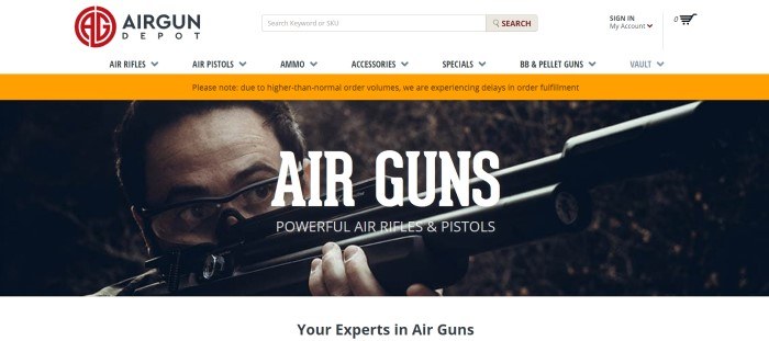 This screenshot of the home page for Airgun Depot has a white header and navigation bar, an orange announcement bar, and a large photo of a man peering through the scope of a gun, along with white text announcing air guns.