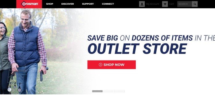 This screenshot of the home page for Crosman has a black and red navigation bar above a photo of a man and a woman in safety goggles walking through a wooded area, smiling, with an airsoft gun in the man's hand, next to dark text that announces the outlet store and a red call to action button.