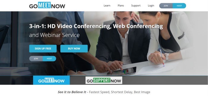 This screenshot of the home page for Go Meet Now has a white navigation bar above a photo of two men and two women focused on the screen of a mobile device on the table in front of them, along with two blue call-to-action buttons and white text inviting customers to find out more about video conferencing and web conferencing.