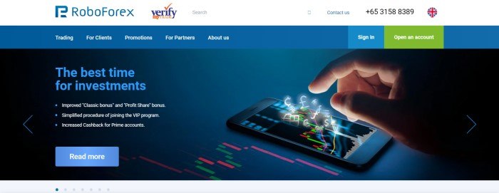 This screenshot of the home page for RoboForex has a white header, a blue navigation bar, and a photo of a man's hand about to tap a mobile device that has electronic currency symbols floating out of the screen, along with blue and white text announcing the best time for investments and a blue call to action button.