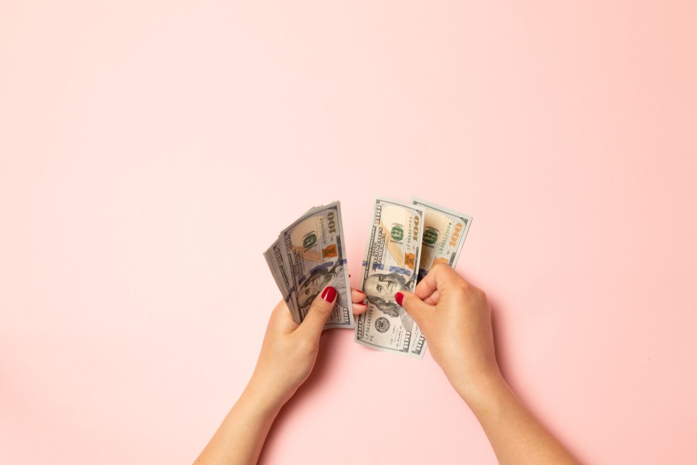 woman with red painted fingernail polish counting 100 bills